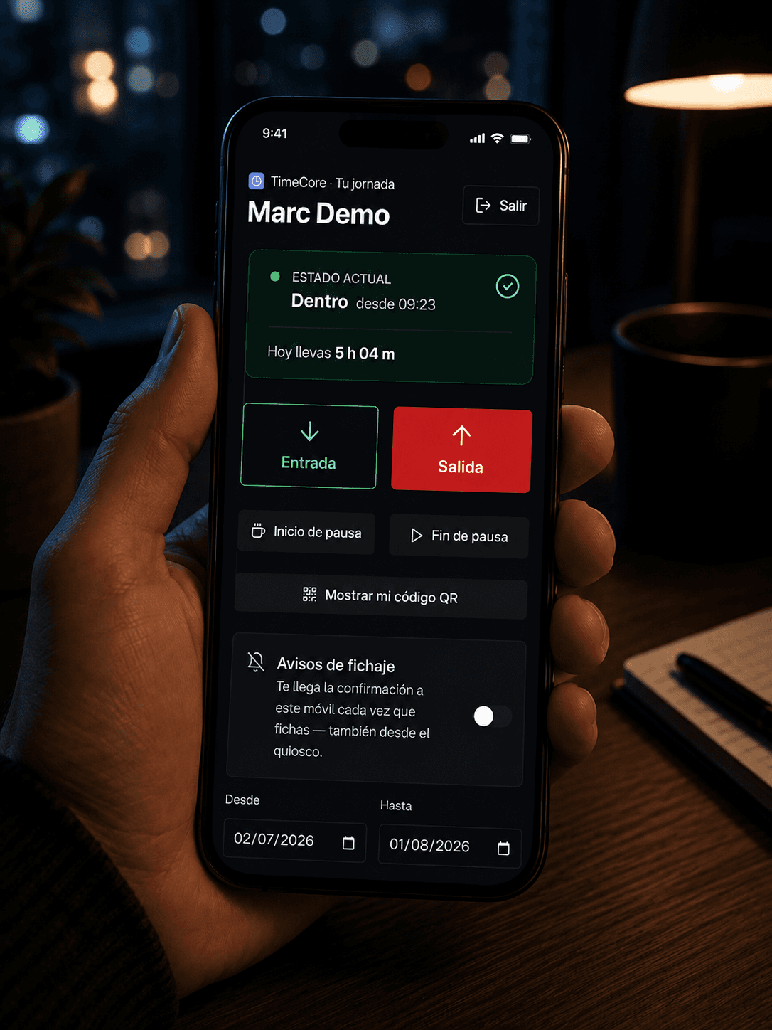 Una mano sostiene un móvil con el portal del trabajador de TimeCore: el nombre de la persona, la tarjeta «Estado actual — Dentro desde 09:23, hoy llevas 5 h 04 m» y los botones de Entrada, Salida, Inicio de pausa, Fin de pausa y «Mostrar mi código QR».