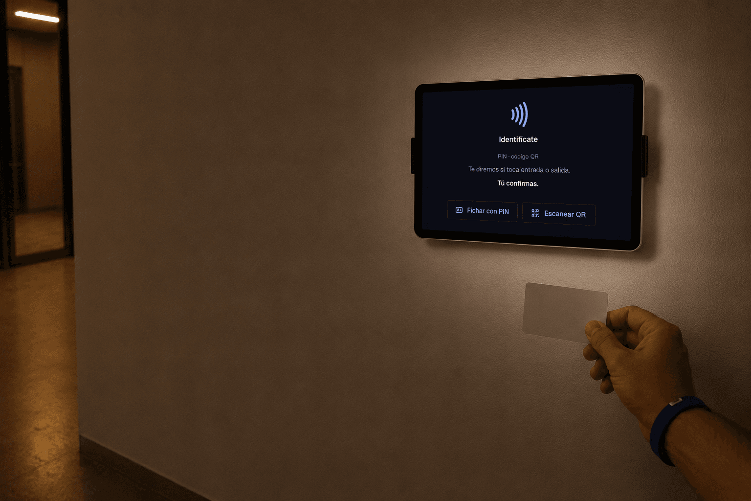 Una tablet montada en la pared junto a la entrada muestra la pantalla de espera del fichador de TimeCore —«Identifícate», «Fichar con PIN» y «Escanear QR»— mientras una mano le acerca una tarjeta lisa.