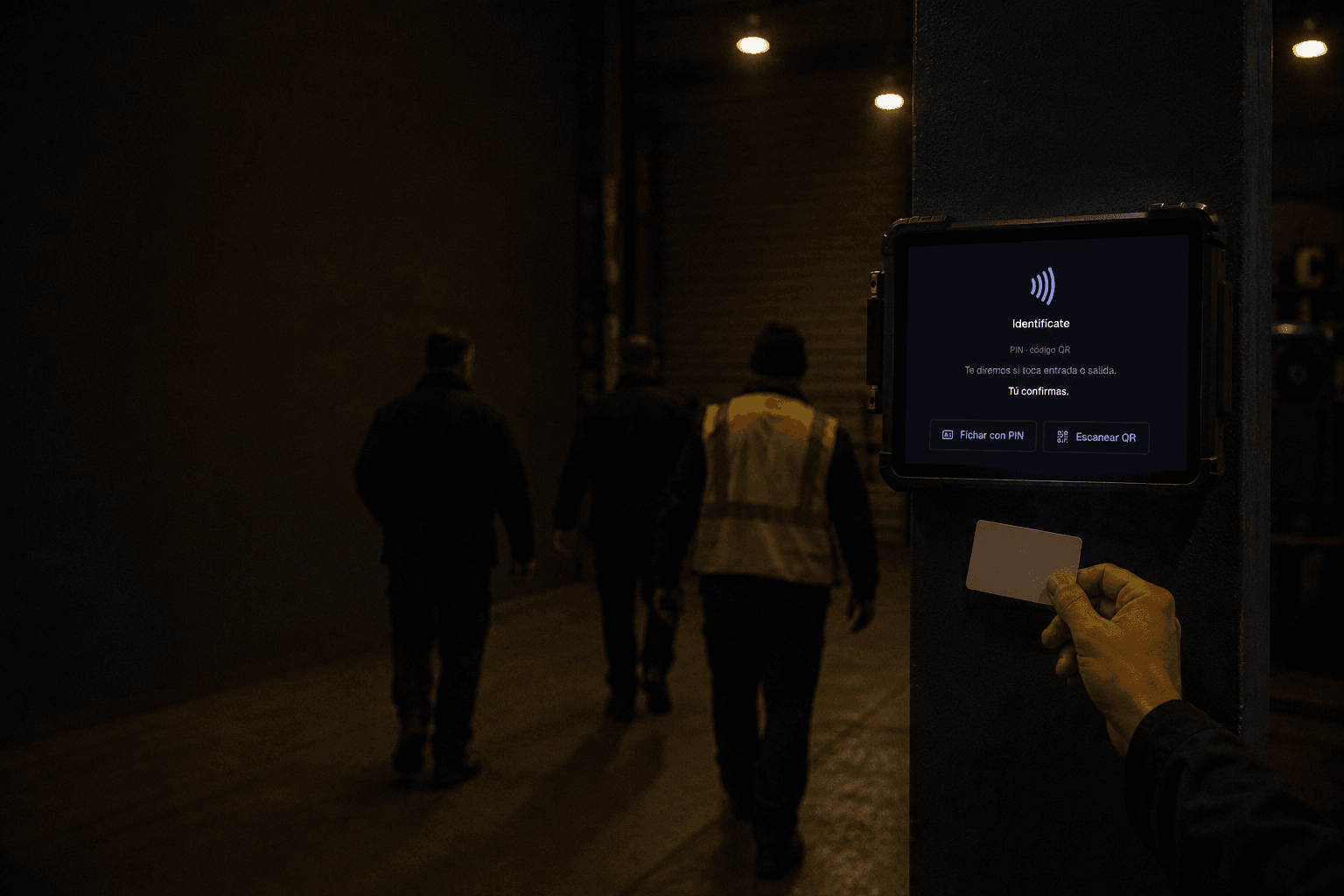 Tres operarios con ropa de trabajo entran a la nave de espaldas a la cámara mientras uno acerca una tarjeta al fichador montado en una columna.